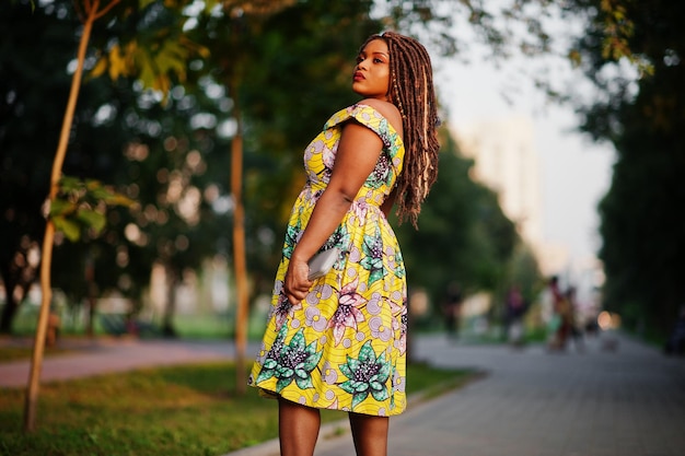 La ragazza afroamericana carina di piccola altezza con i dreadlocks indossa un vestito giallo colorato in posa al tramonto