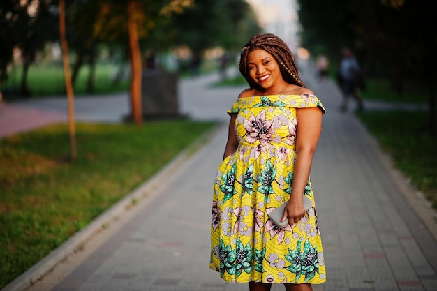 Cute small height african american girl with dreadlocks wear at coloured yellow dress posed at sunset