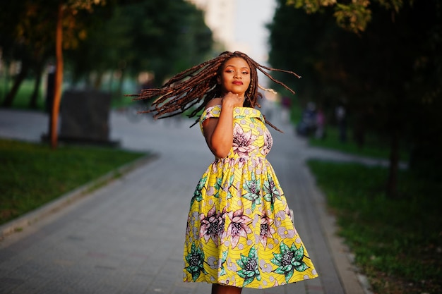 Симпатичная африканская американка маленького роста с дредами в цветном желтом платье, позирующем на закате