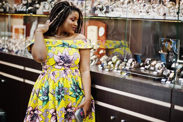 Симпатичная африканская американка маленького роста с дредами в цветном желтом платье в магазине часов в торговом центре