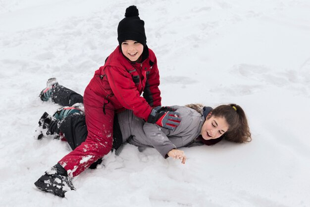 Cute smiling boy playing with her sister on snowy land at winter day