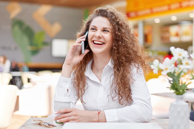 Cute smiling curly woman enjoys phone conversation with best friend