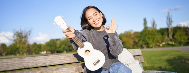 免費 Photo 可愛微笑的女孩展示了"ok"的標誌,她的新烏克萊爾坐在公園的長上,推音樂
