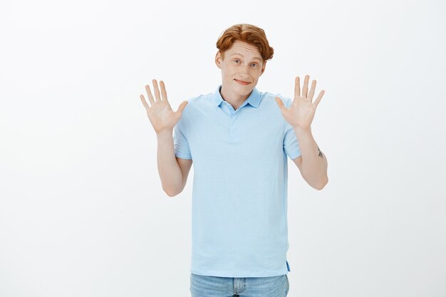 Cute smiling redhead man apologising, raising hands up unaware, don't know