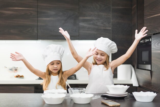Милые улыбающиеся сестры в кухне, наслаждаясь во время приготовления пищи