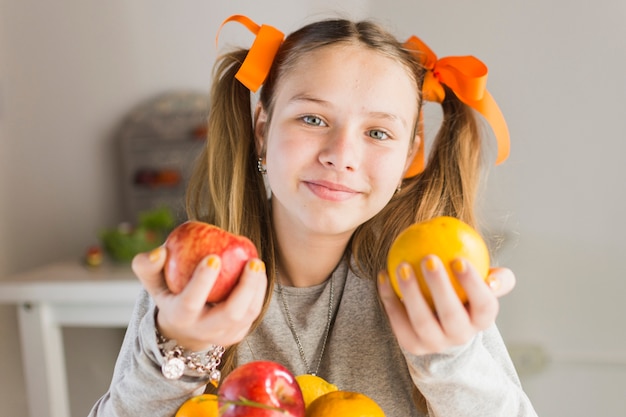 Cute smiling woman holding red apple and an orange in hands