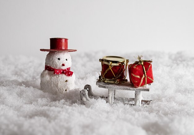 Cute snowman toy, sleigh, and colorful gift boxes in the snow