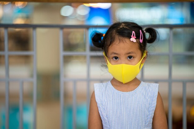 Cute Southeast Asian female child wearing a yellow protection face mask at a shopping mall