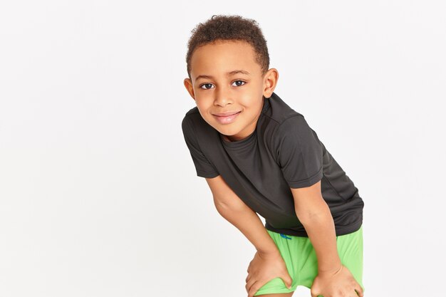 Cute sschoolboy in sportswear exercising at physical education class, holding hands on thighs