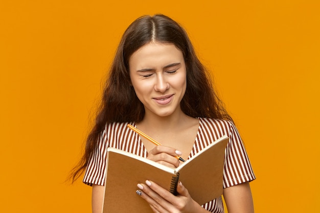 Cute student girl with loose long hair keeping eyes closed, laughing at something funny