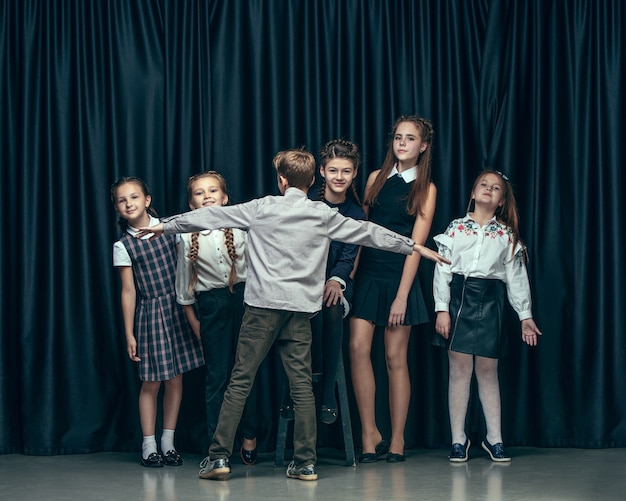 Cute stylish children on dark studio background. The beautiful teen girls and boy standing together