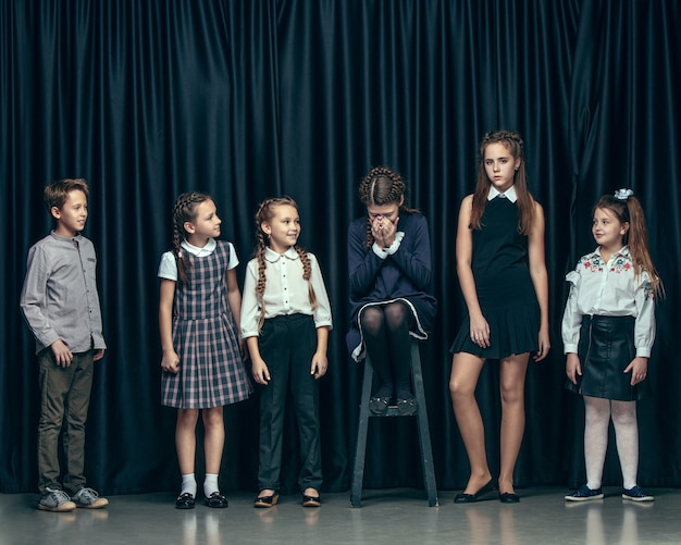 Cute stylish children on dark studio background. The beautiful teen girls and boy standing together