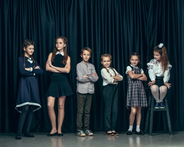 Cute stylish children on dark studio background. The beautiful teen girls and boy standing together