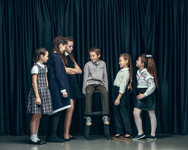 Cute stylish children on dark studio. The beautiful teen girls and boy standing together