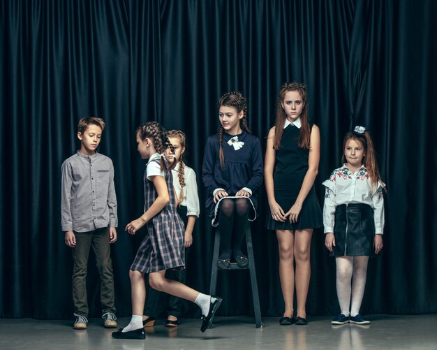 Cute stylish children on dark studio. The beautiful teen girls and boy standing together