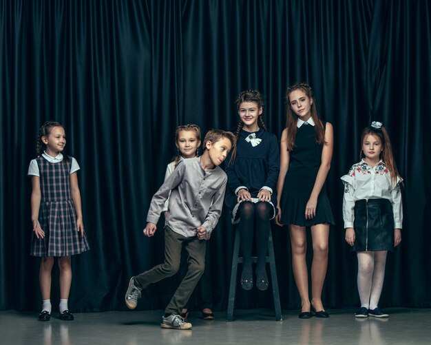 Cute stylish children on dark studio. The beautiful teen girls and boy standing together