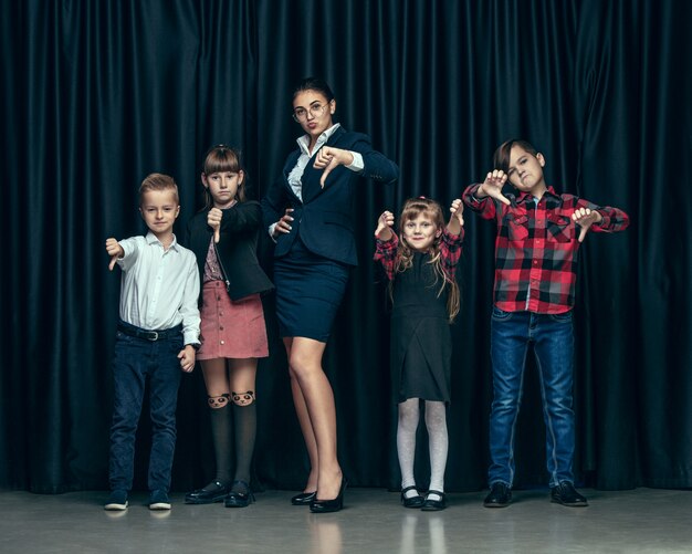 Cute stylish children on dark studio wall. The beautiful teen girls and a boy standing together