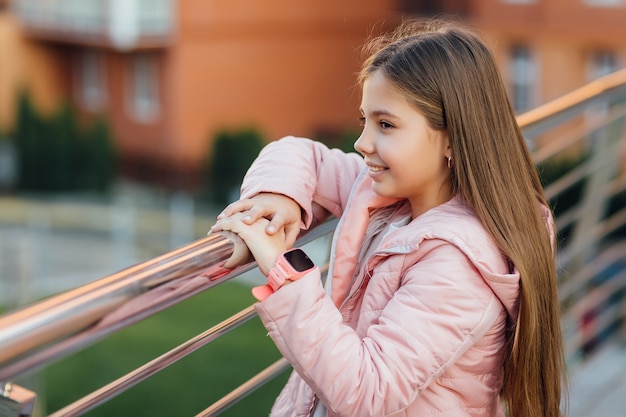 Ragazza carina ed elegante con un moderno orologio intelligente che cammina dopo la scuola vicino alla città