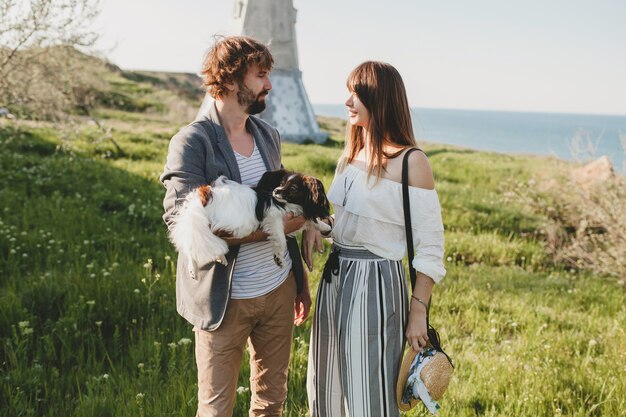 Cute stylish hipster couple in love walking with dog in countryside, summer style boho fashion, romantic