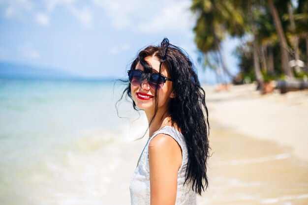 Cute summer fashion portrait of beauty brunette woman having fun on the beach, dancing and smiling