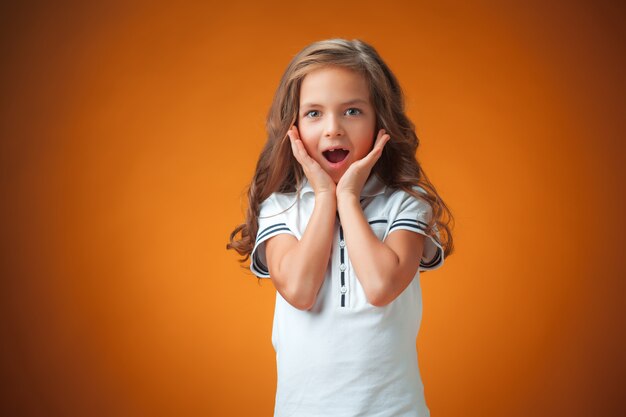 The cute surprised little girl on orange wall