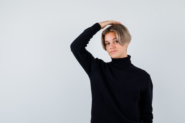 Cute teen boy in black turtleneck sweater with hand on head and looking intelligent
