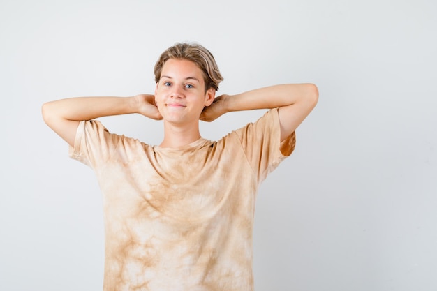 Foto gratuita ragazzo adolescente carino che tiene le mani dietro la testa in maglietta e sembra allegro, vista frontale.