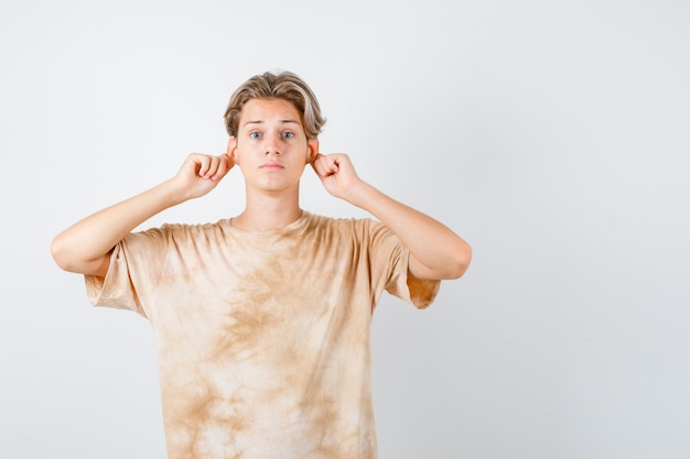 Cute teen boy pulling down his earlobes in t-shirt and looking scared. front view.