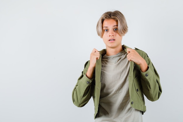 Free photo cute teen boy pulling his open jacket in green jacket and looking scared , front view.