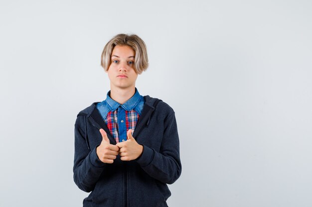 Cute teen boy in shirt, hoodie showing double thumbs up and looking pleased , front view.