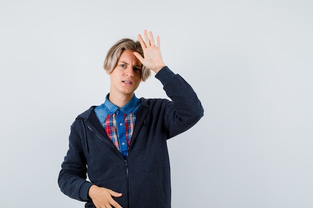 Cute teen boy in shirt, hoodie showing palm and looking displeased , front view.