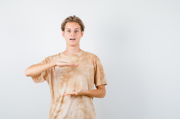 Cute teen boy showing size sign in t-shirt and looking wondered , front view.