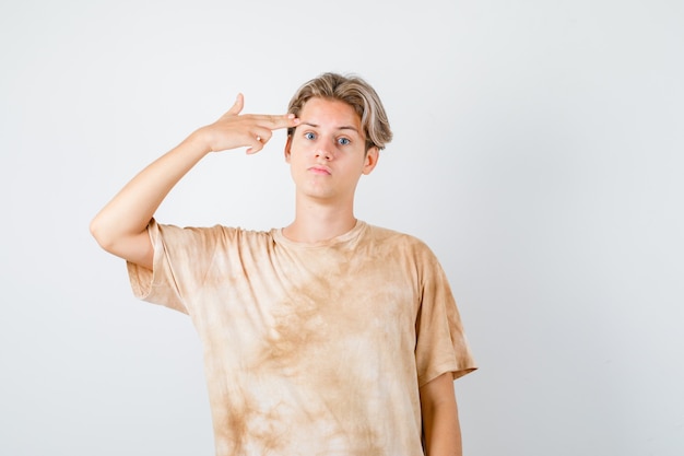 Милый подросток мальчик показывает жест самоубийства в футболке и выглядит подавленным, вид спереди.