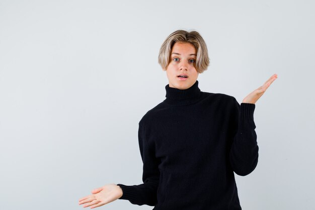 Cute teen boy in turtleneck sweater showing helpless gesture and looking confused