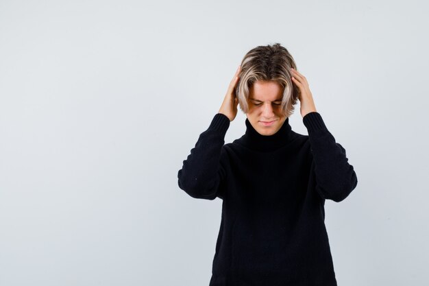 Cute teen boy with hands on head in black turtleneck sweater and looking fatigued. front view.