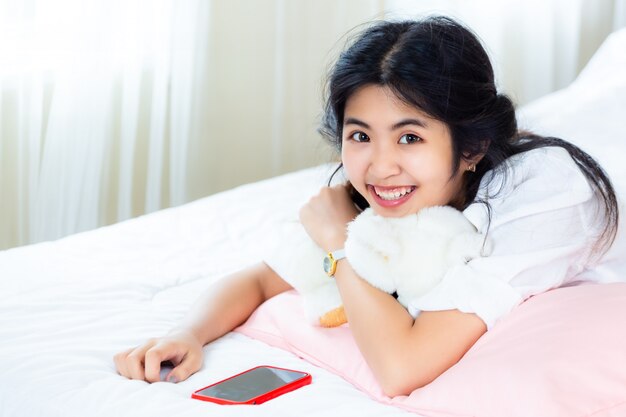 ベッドの上のスマートフォンでうれしそうなかわいい10代女性