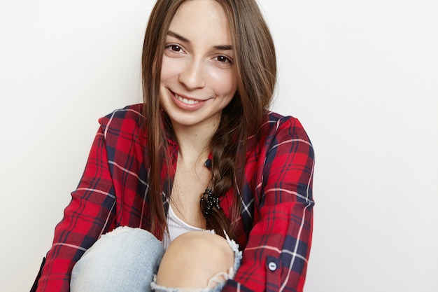 Cute teenage girl looking at camera and smiling shyly embracing her knees