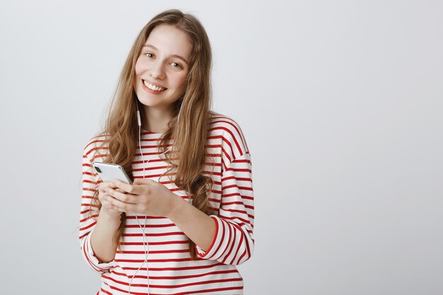 Милая девочка-подросток с помощью мобильного телефона и прослушивания музыки в наушниках