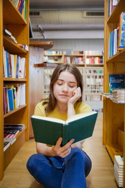 Cute teenager reading between bookcases