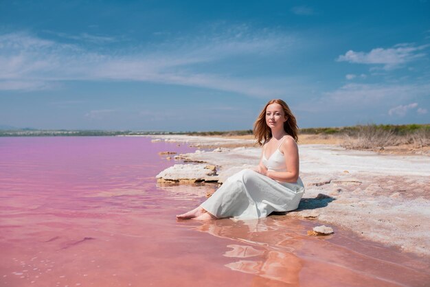 Милая девушка подростка нося белое платье сидя на изумительном розовом озере