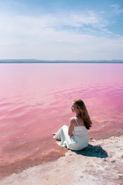 驚くべきピンクの湖の上に座って白いドレスを着ているかわいい10代の女性