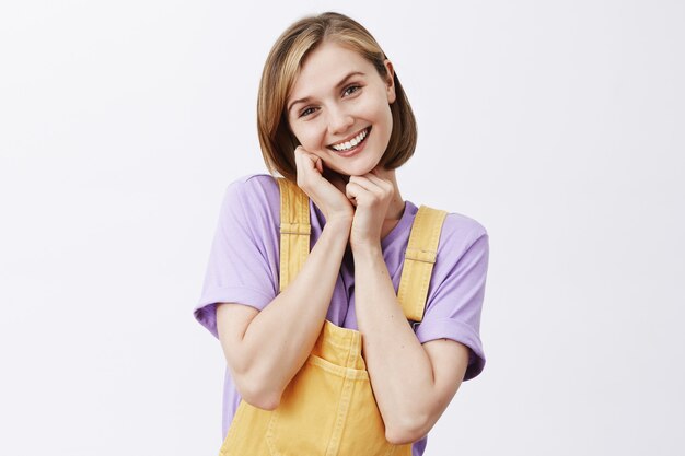 Cute and tender young woman smiling and blushing coquettish over white wall