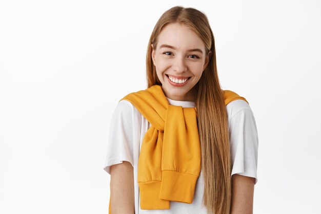 Cute timid girl with beautiful white smile standing shy and silly looking at camera blushing standing against white background