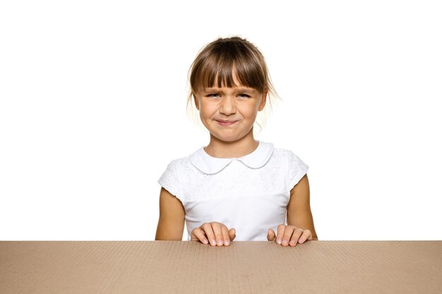 Cute and upset little girl on biggest postal package. Disappointed young female model on top of cardboard box looking inside.