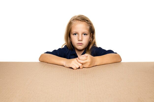 Cute and upset little girl opening the biggest package. Disappointed young female model on top of cardboard box