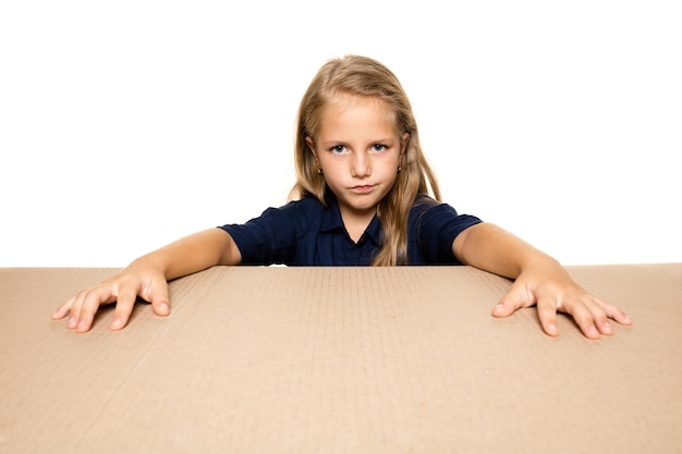 Cute and upset little girl opening the biggest postal package. Disappointed young female model on top of cardboard box