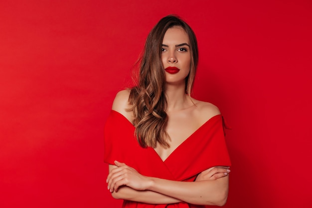 Cute wavy haired woman with red bright lipstick in stylish red sundress smiling and posing on isolated