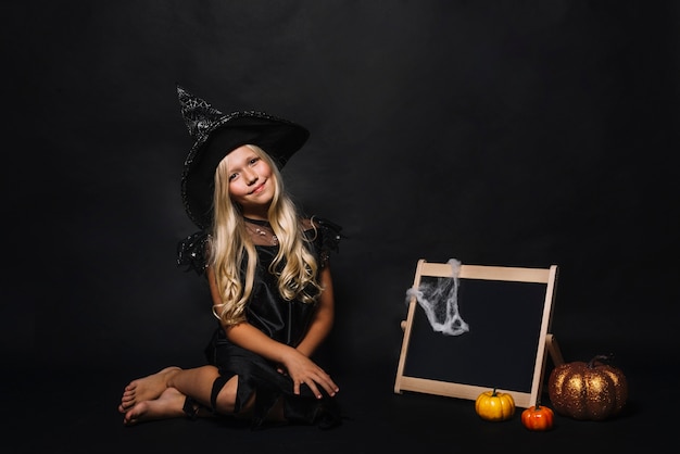 Cute witch near blackboard and pumpkins