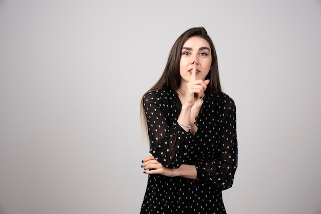 Cute woman in black dress making silence sign.