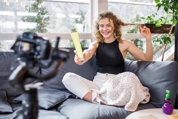 Cute woman blogger during fashion blog, holding shampoo for the head